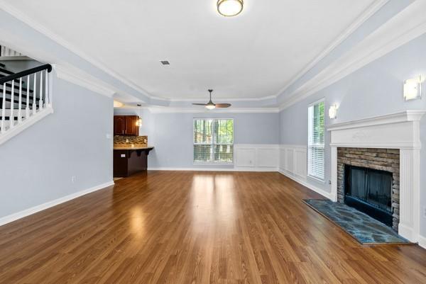 unfurnished living room with ceiling fan, ornamental molding, a fireplace, wood finished floors, and stairway
