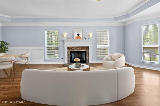 living area with crown molding, a stone fireplace, wood finished floors, and baseboards