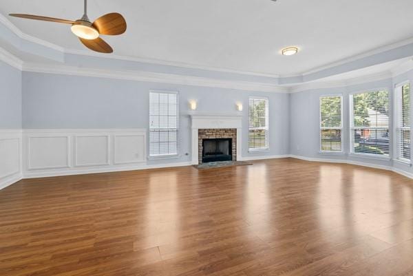 unfurnished living room with a tray ceiling, crown molding, wood finished floors, ceiling fan, and a fireplace