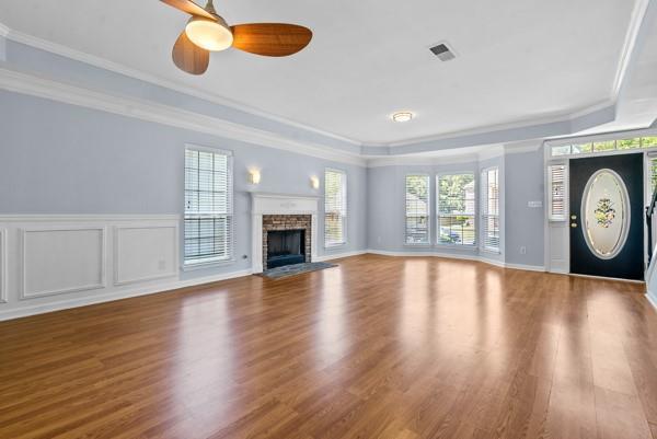 unfurnished living room featuring wood finished floors, a ceiling fan, a brick fireplace, crown molding, and a raised ceiling