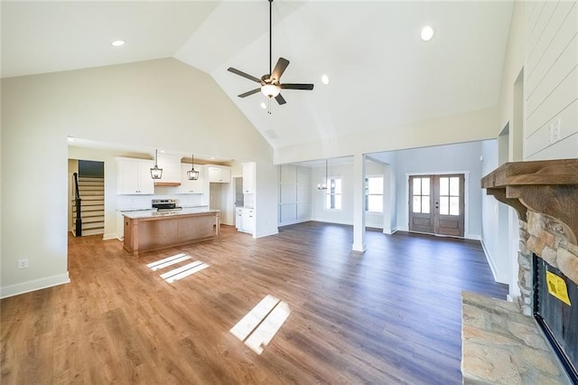 unfurnished living room with ceiling fan, high vaulted ceiling, a fireplace, stairs, and light wood finished floors