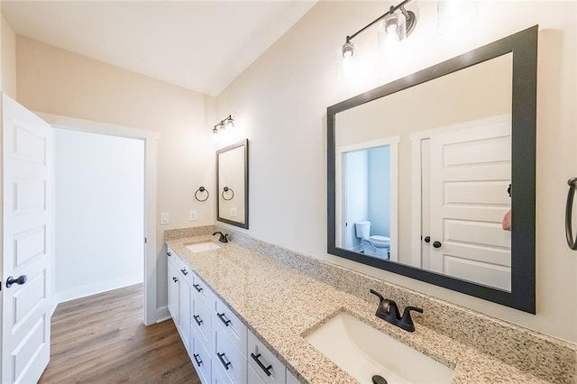 full bath with double vanity, a sink, toilet, and wood finished floors