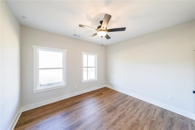 unfurnished room with visible vents, wood finished floors, a ceiling fan, and baseboards