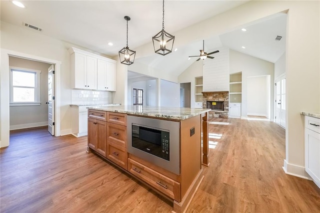 kitchen with a fireplace, visible vents, white cabinets, light wood-type flooring, and stainless steel microwave