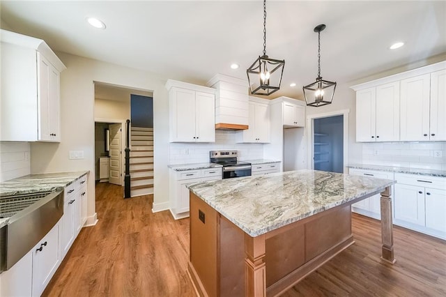 kitchen with light wood-style floors, stainless steel range with electric cooktop, premium range hood, and white cabinetry