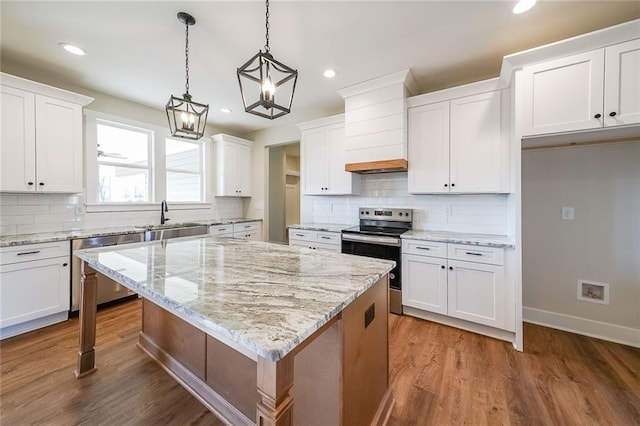 kitchen with wood finished floors, a sink, white cabinets, appliances with stainless steel finishes, and a center island