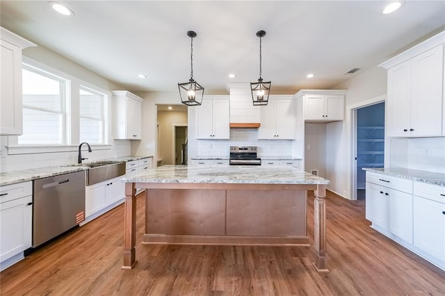 kitchen with a sink, stainless steel appliances, wood finished floors, and white cabinetry