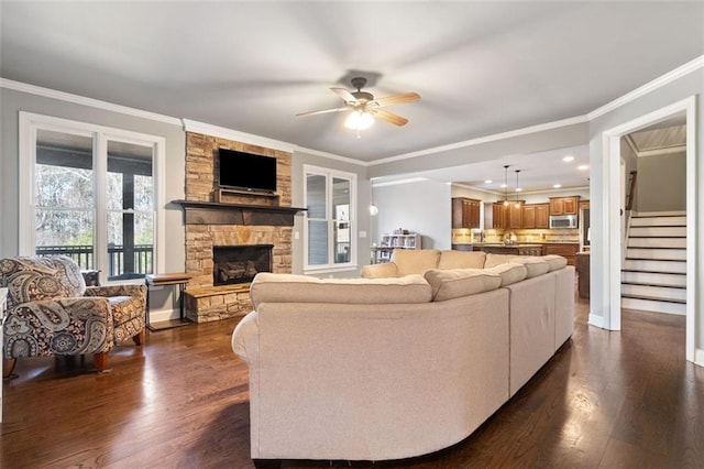 living room featuring dark hardwood / wood-style floors, ceiling fan, crown molding, and a stone fireplace