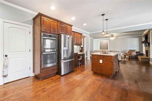 kitchen featuring a stone fireplace, stainless steel appliances, hanging light fixtures, a center island, and light stone counters