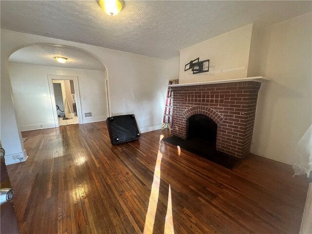 1165 Oak St SW, Atlanta, GA 30310 - unfurnished living room featuring arched walkways, wood-type flooring, a brick fireplace, a textured ceiling, and baseboards
