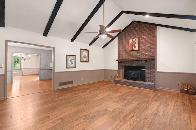 unfurnished living room featuring a brick fireplace, ceiling fan with notable chandelier, lofted ceiling with beams, and light hardwood / wood-style floors