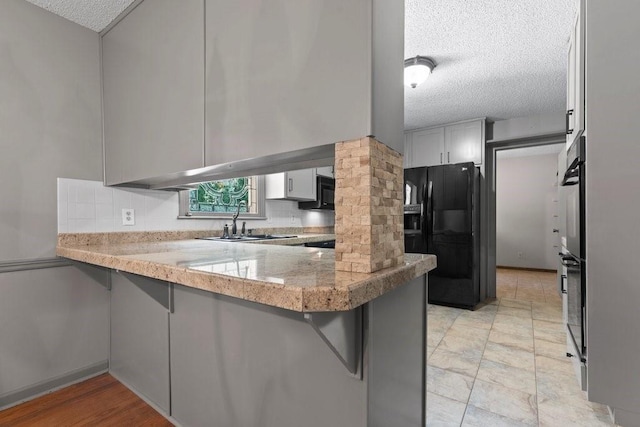 kitchen with tasteful backsplash, kitchen peninsula, sink, and black appliances