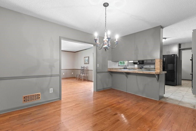 kitchen featuring a breakfast bar, gray cabinetry, hanging light fixtures, black fridge, and kitchen peninsula