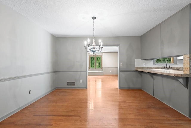 unfurnished dining area with an inviting chandelier, sink, light hardwood / wood-style floors, and a textured ceiling