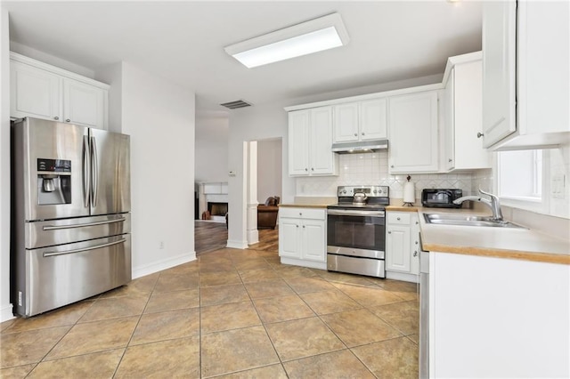 kitchen with appliances with stainless steel finishes, light countertops, under cabinet range hood, white cabinetry, and a sink