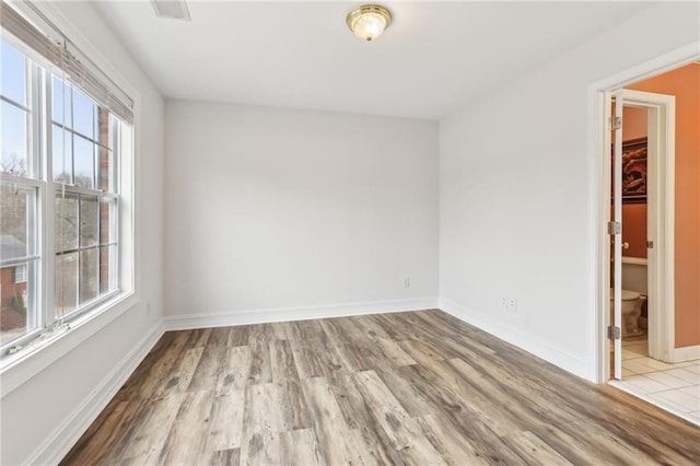 spare room featuring light wood finished floors, visible vents, and baseboards