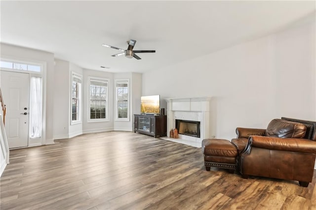 living room featuring a high end fireplace, ceiling fan, baseboards, and wood finished floors