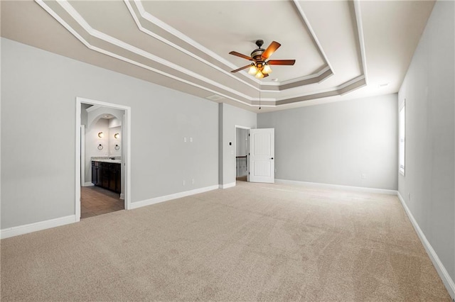 unfurnished bedroom featuring crown molding, a tray ceiling, ensuite bath, and light colored carpet