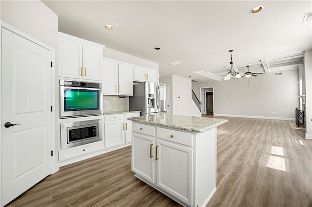 kitchen with stainless steel appliances, a center island, light stone countertops, white cabinets, and decorative backsplash