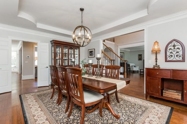 dining area with a raised ceiling, stairway, ornamental molding, wood finished floors, and a notable chandelier