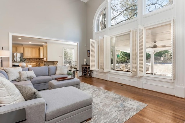 living room with visible vents, ceiling fan, a towering ceiling, and wood finished floors