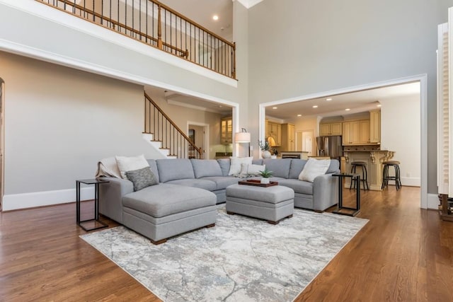 living area with recessed lighting, a high ceiling, wood finished floors, baseboards, and stairway