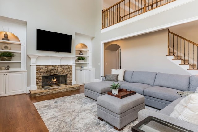 living room featuring built in shelves, a fireplace, stairway, a high ceiling, and wood finished floors