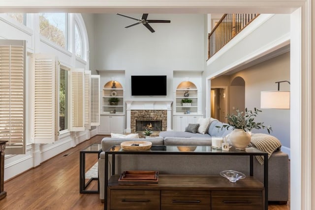 living area with a high ceiling, a ceiling fan, wood finished floors, and a stone fireplace