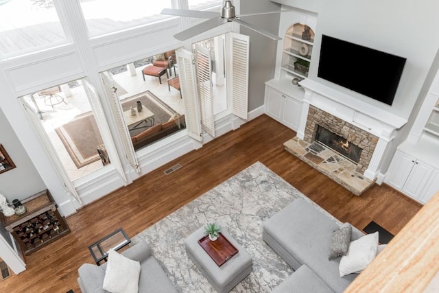 living area with a stone fireplace, wood finished floors, visible vents, and a ceiling fan