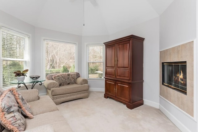 living area featuring lofted ceiling, a healthy amount of sunlight, a tile fireplace, and light colored carpet