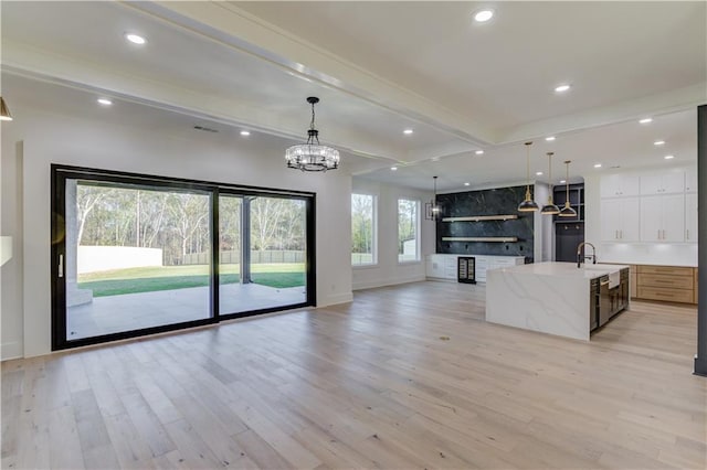 unfurnished living room with a chandelier, light hardwood / wood-style floors, beamed ceiling, and sink