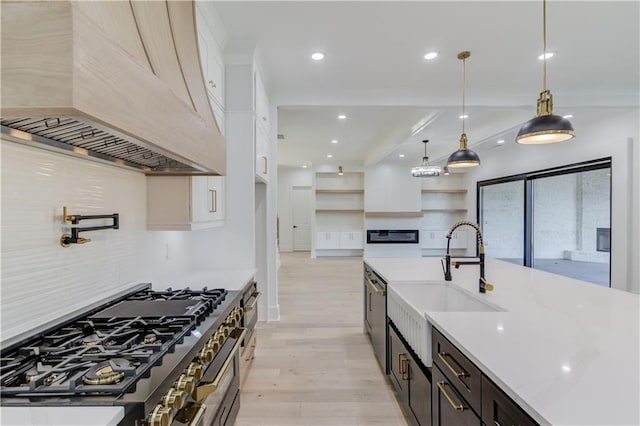 kitchen featuring custom exhaust hood, stainless steel appliances, sink, light hardwood / wood-style floors, and hanging light fixtures