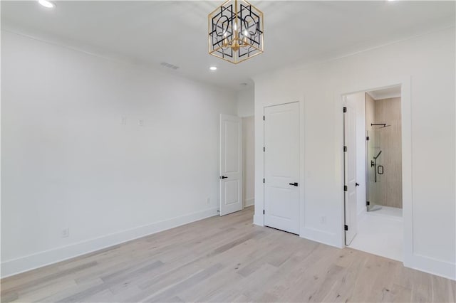 unfurnished bedroom featuring a chandelier, light wood-type flooring, and connected bathroom