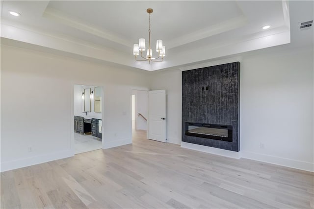 unfurnished living room with a raised ceiling, a large fireplace, a notable chandelier, and light wood-type flooring