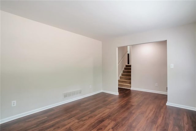 empty room with stairs, dark wood-style flooring, and baseboards