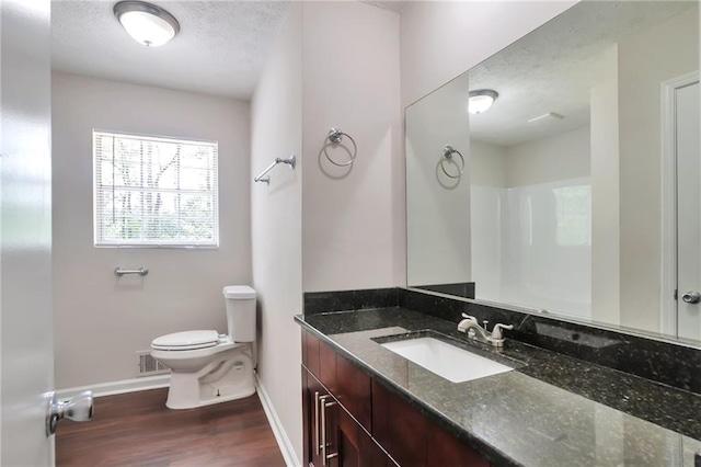 bathroom featuring baseboards, wood finished floors, toilet, a textured ceiling, and vanity