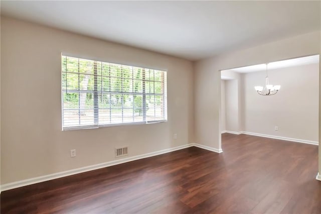 spare room featuring a chandelier, dark wood-style flooring, and baseboards
