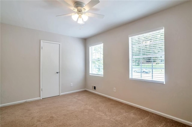 spare room with light colored carpet, a ceiling fan, and baseboards
