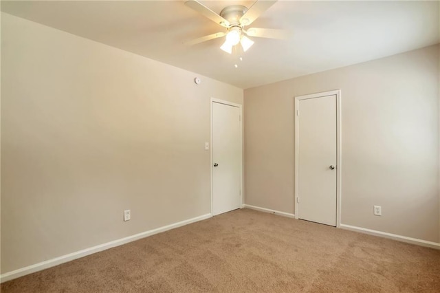 empty room featuring ceiling fan, light colored carpet, and baseboards