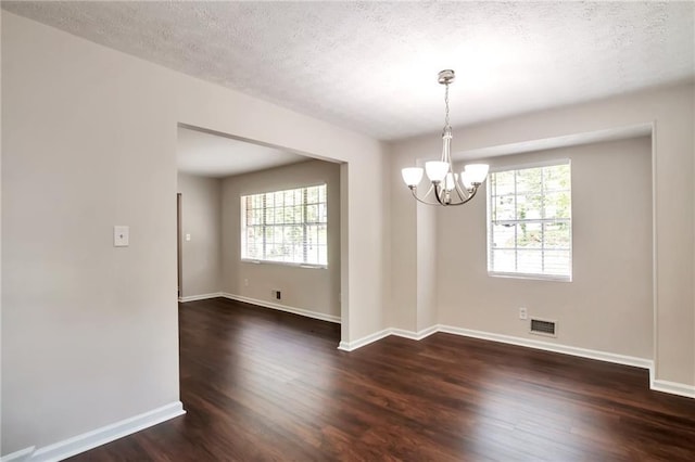 unfurnished dining area with a chandelier, dark wood-style flooring, healthy amount of natural light, and a textured ceiling
