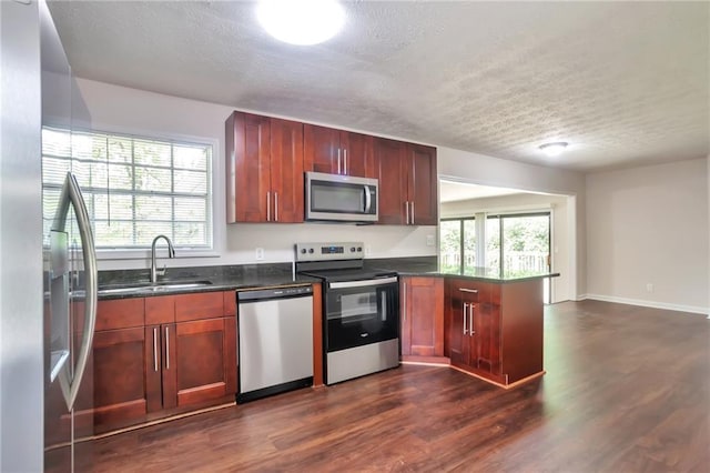 kitchen featuring appliances with stainless steel finishes, a sink, a textured ceiling, a peninsula, and dark wood-style floors