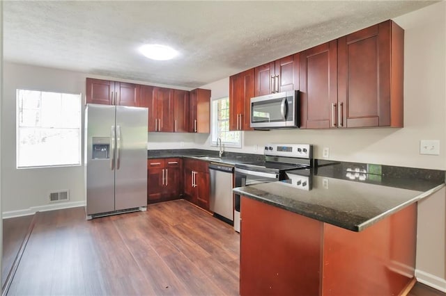 kitchen with appliances with stainless steel finishes, dark wood-style flooring, a peninsula, reddish brown cabinets, and a textured ceiling