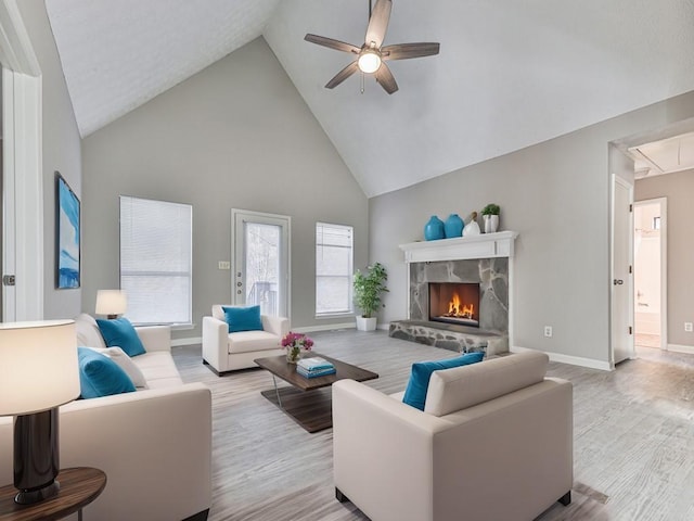 living room featuring a fireplace, light hardwood / wood-style flooring, high vaulted ceiling, and ceiling fan