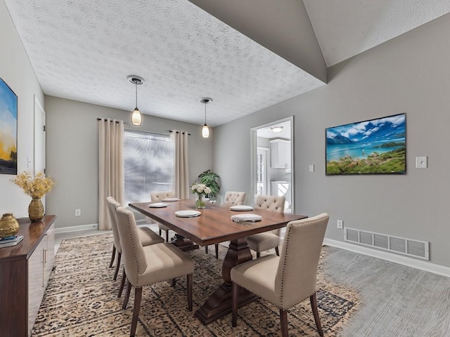 dining room featuring wood-type flooring, a textured ceiling, and lofted ceiling