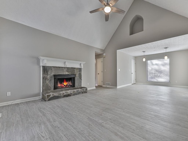 unfurnished living room featuring ceiling fan, light wood-type flooring, a fireplace, and high vaulted ceiling