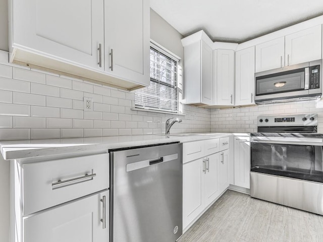 kitchen featuring light wood-type flooring, stainless steel appliances, white cabinetry, and tasteful backsplash