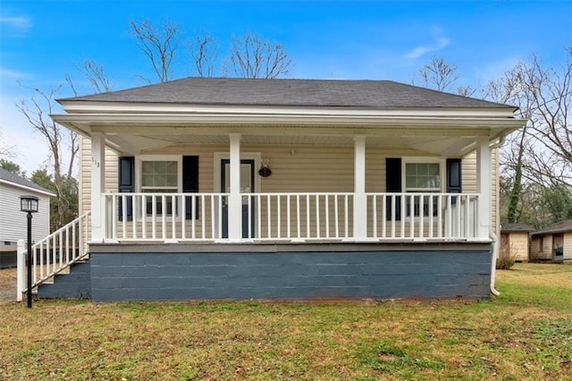 view of front of home with covered porch, a shingled roof, and a front yard