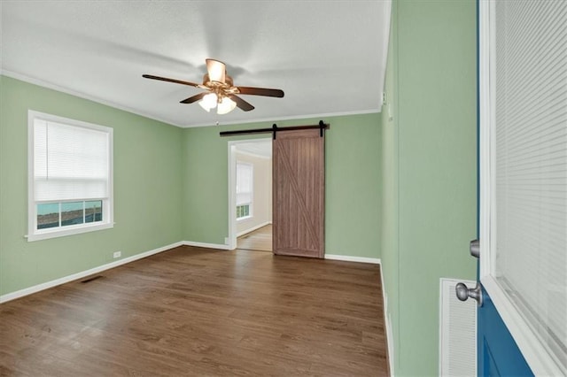 unfurnished room with a barn door, visible vents, dark wood-style flooring, and crown molding