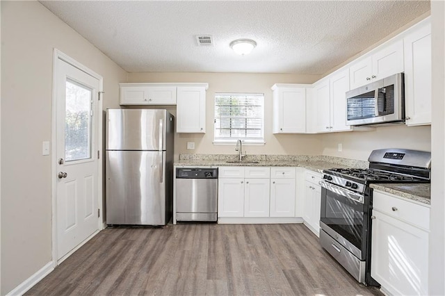 kitchen with sink, light stone counters, white cabinetry, and appliances with stainless steel finishes