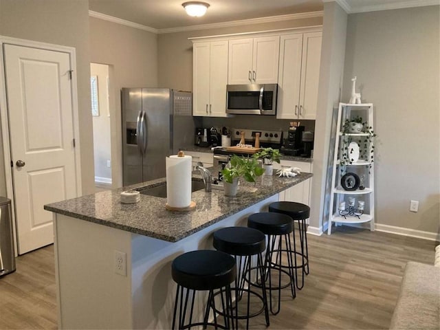 kitchen featuring an island with sink, a breakfast bar area, appliances with stainless steel finishes, wood-type flooring, and white cabinets